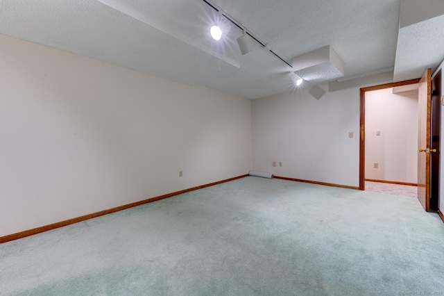 unfurnished room with track lighting, light colored carpet, a textured ceiling, and baseboards