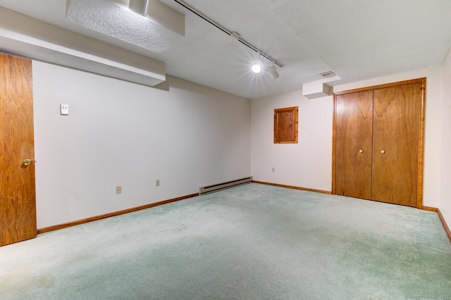 finished basement featuring baseboards, visible vents, light colored carpet, baseboard heating, and track lighting