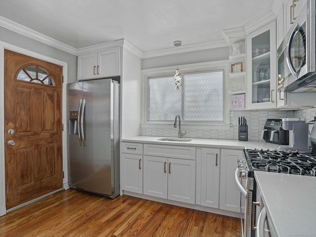 kitchen with ornamental molding, appliances with stainless steel finishes, wood finished floors, and a sink