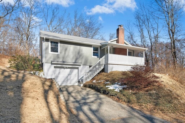 view of front of property featuring covered porch, driveway, a chimney, and an attached garage