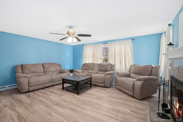 living room featuring a tile fireplace, ceiling fan, light wood finished floors, and a baseboard radiator