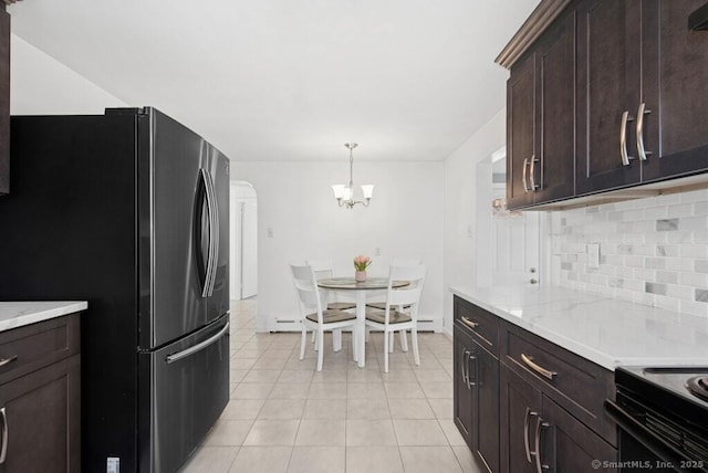 kitchen with dark brown cabinetry, light tile patterned floors, arched walkways, decorative backsplash, and freestanding refrigerator