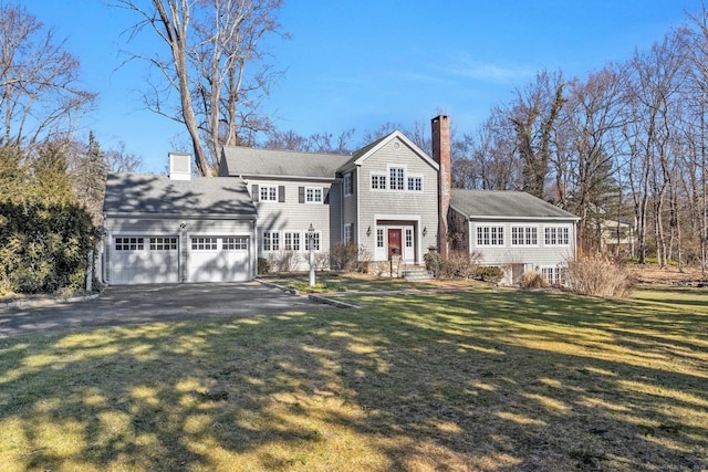 view of front of property featuring a garage, aphalt driveway, a chimney, and a front yard