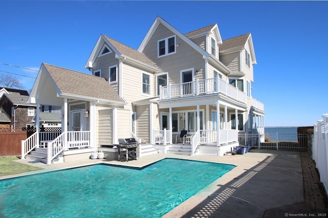 rear view of property with a balcony, a shingled roof, fence, and a fenced in pool