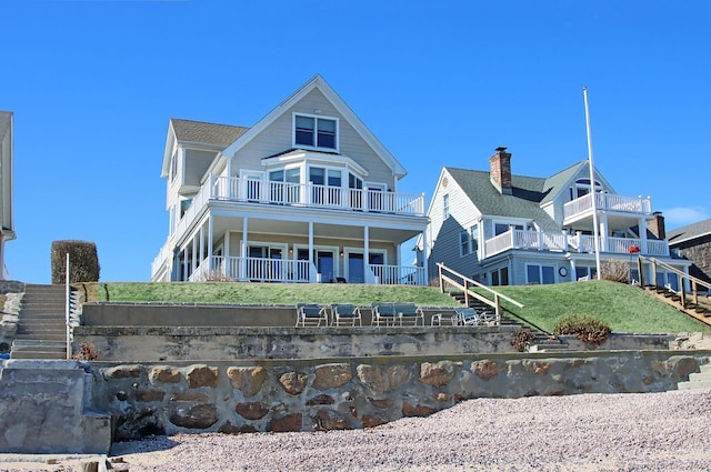 rear view of property featuring a porch, a lawn, and a balcony