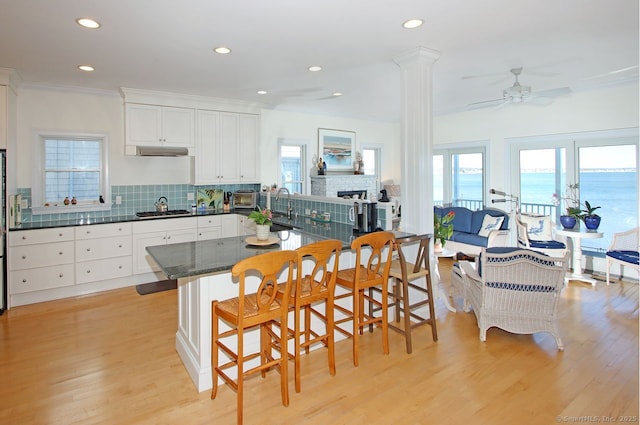 kitchen featuring a breakfast bar area, stainless steel gas cooktop, a water view, white cabinets, and backsplash