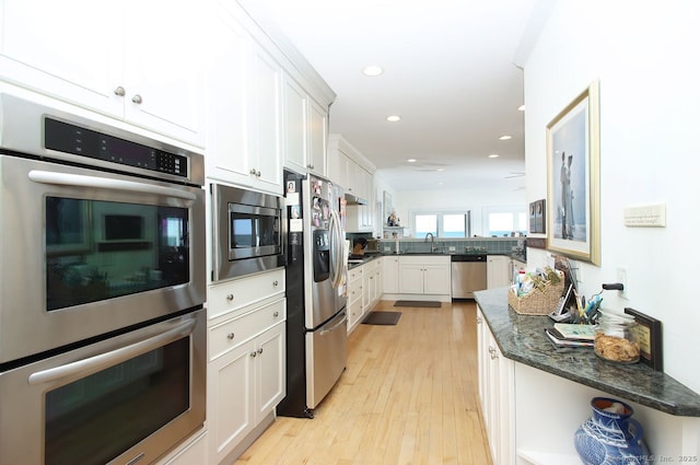 kitchen with appliances with stainless steel finishes, white cabinets, light wood-type flooring, dark stone counters, and a peninsula