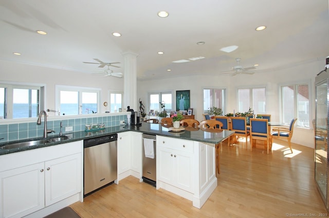 kitchen featuring a water view, a peninsula, stainless steel dishwasher, white cabinetry, and a sink