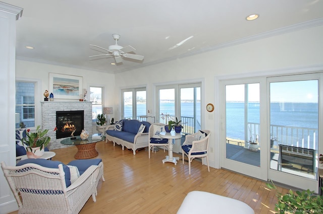 sunroom featuring a water view, a fireplace, and a ceiling fan