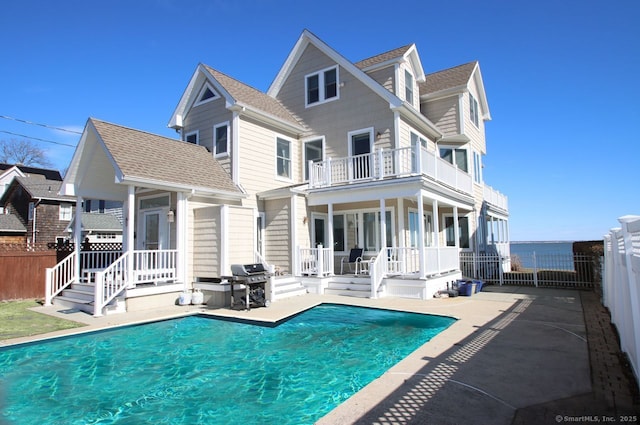 back of property with a shingled roof, fence private yard, a balcony, and a fenced in pool