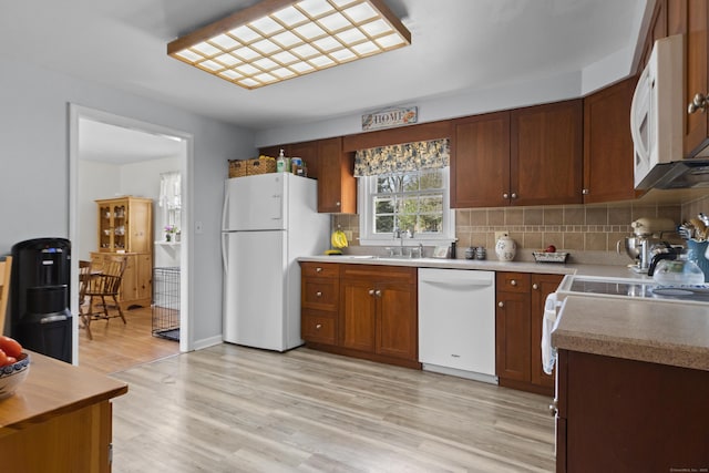 kitchen featuring a sink, white appliances, decorative backsplash, and light wood finished floors