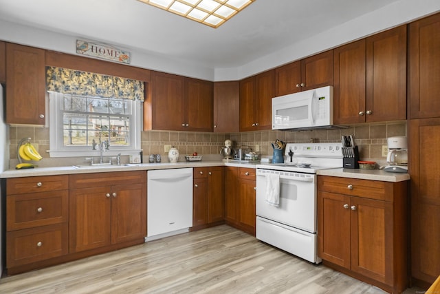 kitchen with light countertops, white appliances, a sink, and light wood-style floors