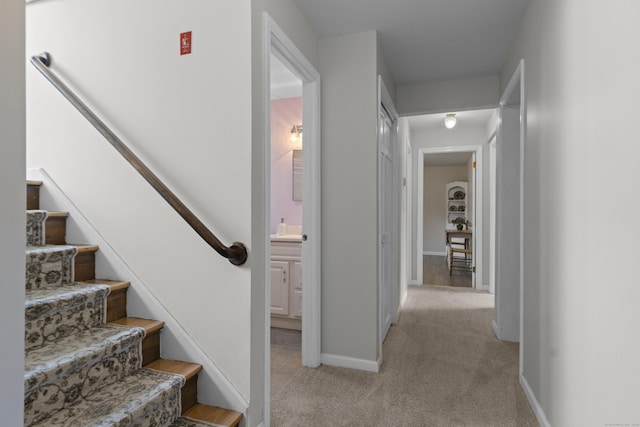 hall featuring light carpet, stairway, and baseboards