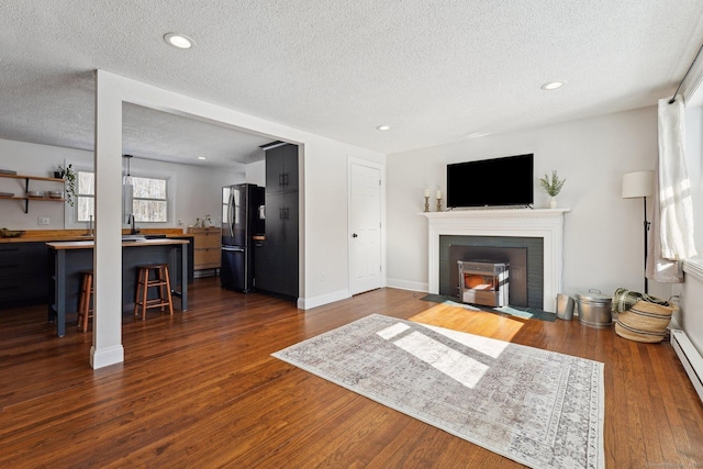 living area featuring dark wood-style floors, recessed lighting, a fireplace with flush hearth, a textured ceiling, and baseboards