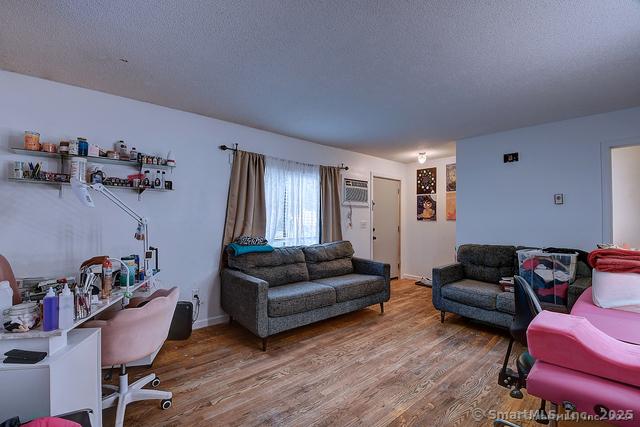 living area with a textured ceiling, an AC wall unit, and wood finished floors