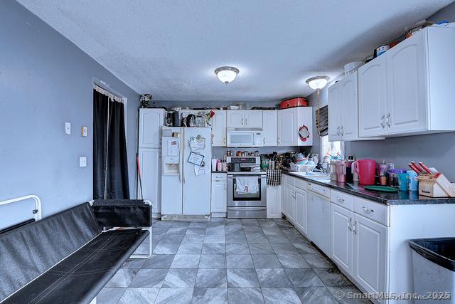 kitchen featuring dark countertops, white appliances, and white cabinetry