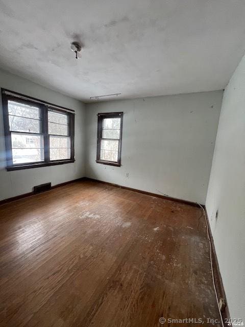 spare room with baseboards, visible vents, and wood finished floors