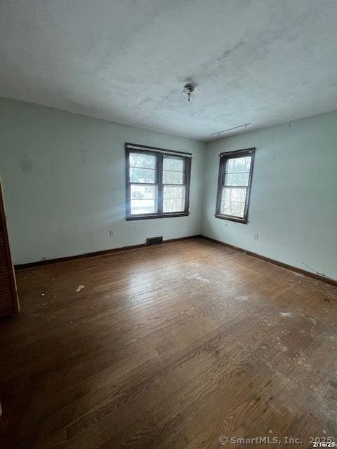 unfurnished room with dark wood-style floors, baseboards, visible vents, and a textured ceiling