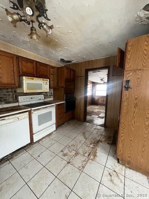 kitchen with white appliances, tasteful backsplash, wooden walls, brown cabinets, and a textured ceiling