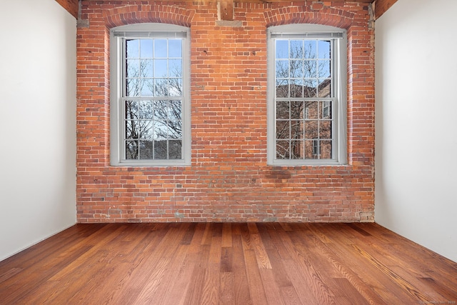 spare room featuring brick wall and wood finished floors