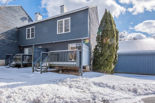 snow covered back of property with a chimney and a wooden deck