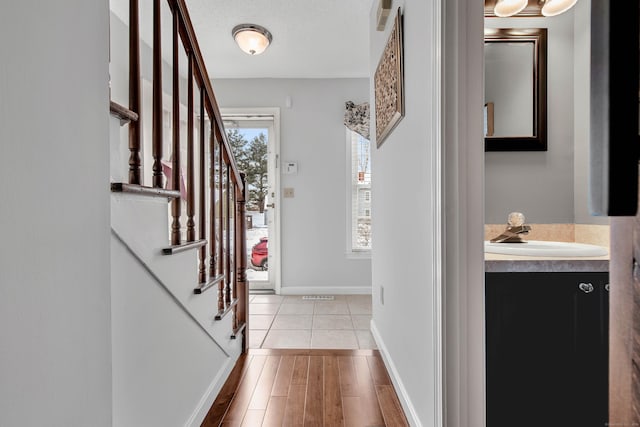 foyer entrance featuring light wood-type flooring, stairway, baseboards, and a textured ceiling