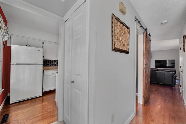 corridor with visible vents, a barn door, a textured ceiling, baseboards, and hardwood / wood-style flooring