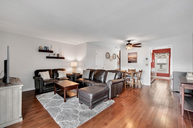 living room featuring dark wood-style floors, a ceiling fan, and baseboards