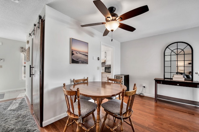 dining space featuring ceiling fan, a barn door, wood-type flooring, and a textured ceiling