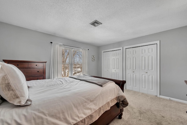 bedroom featuring baseboards, visible vents, carpet, a textured ceiling, and two closets