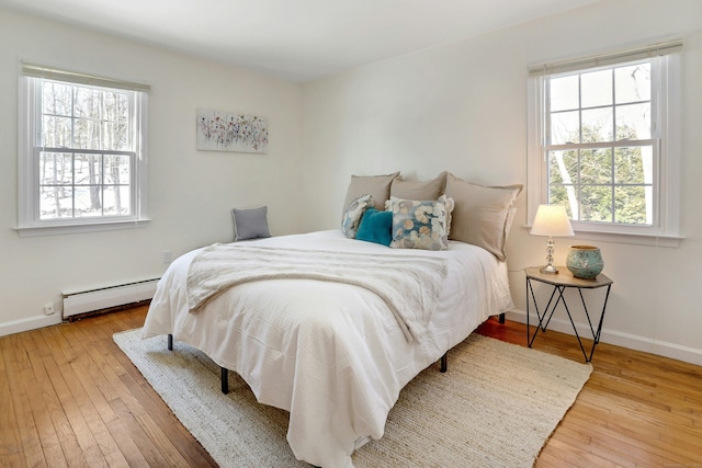 bedroom featuring a baseboard heating unit, wood-type flooring, and baseboards