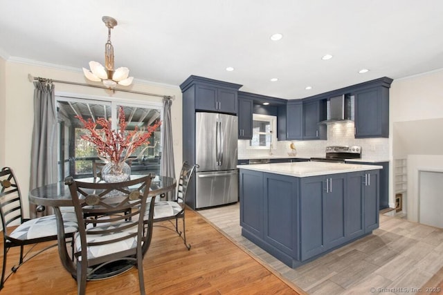 kitchen featuring decorative light fixtures, blue cabinetry, stainless steel appliances, crown molding, and wall chimney range hood