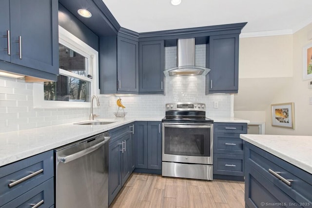 kitchen with stainless steel appliances, a sink, wall chimney range hood, blue cabinetry, and crown molding