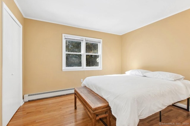 bedroom featuring light wood finished floors, ornamental molding, baseboard heating, and a closet