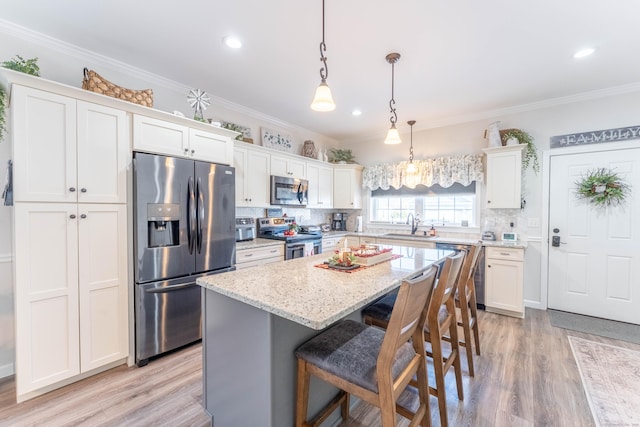 kitchen with stainless steel appliances, a center island, white cabinets, light stone countertops, and crown molding