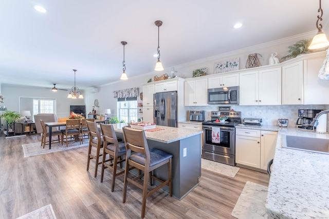 kitchen featuring white cabinets, appliances with stainless steel finishes, a center island, hanging light fixtures, and a sink