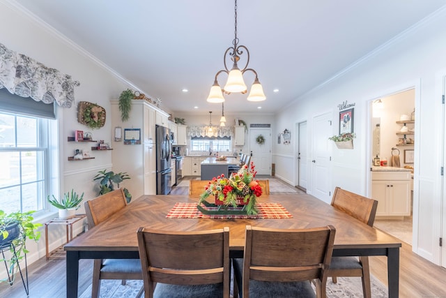 dining space with ornamental molding, light wood finished floors, plenty of natural light, and a notable chandelier