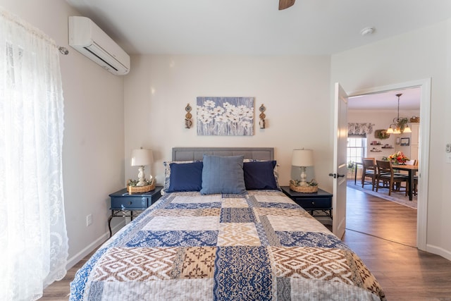 bedroom featuring a wall unit AC, baseboards, and wood finished floors