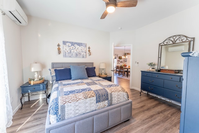 bedroom with an AC wall unit, baseboards, and wood finished floors