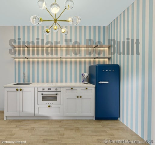 kitchen featuring oven, a sink, wallpapered walls, white cabinets, and light wood finished floors