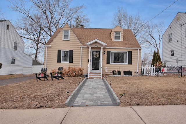 new england style home featuring roof with shingles and fence