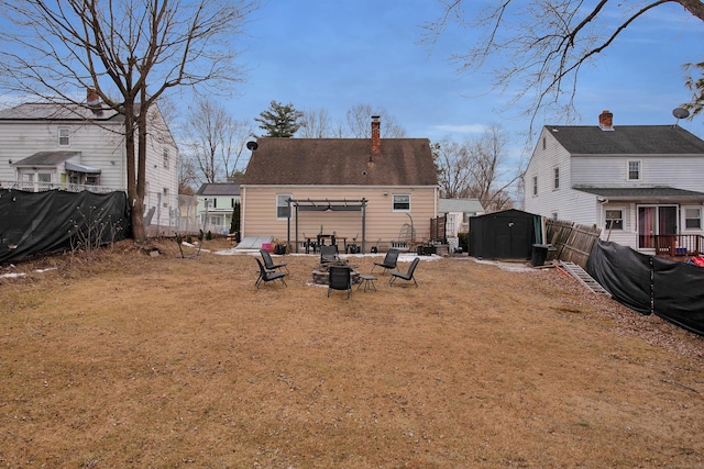 rear view of property featuring an outdoor fire pit, a chimney, an outbuilding, fence, and a storage unit