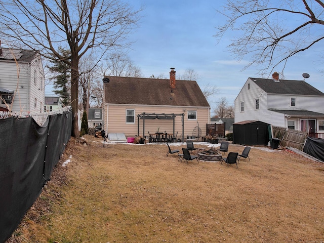 rear view of house with an outbuilding, a fenced backyard, a fire pit, a storage shed, and a chimney