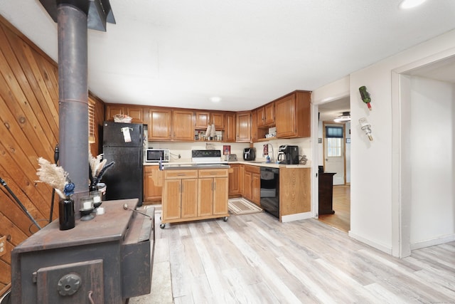 kitchen with wood walls, light wood-style floors, light countertops, black appliances, and a wood stove