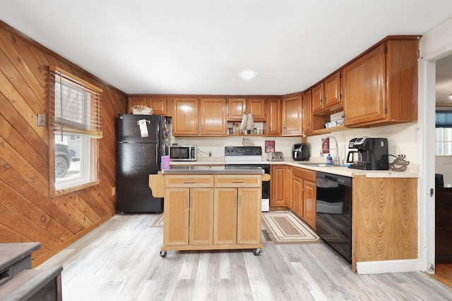 kitchen featuring light wood-type flooring, a sink, wood walls, and black appliances