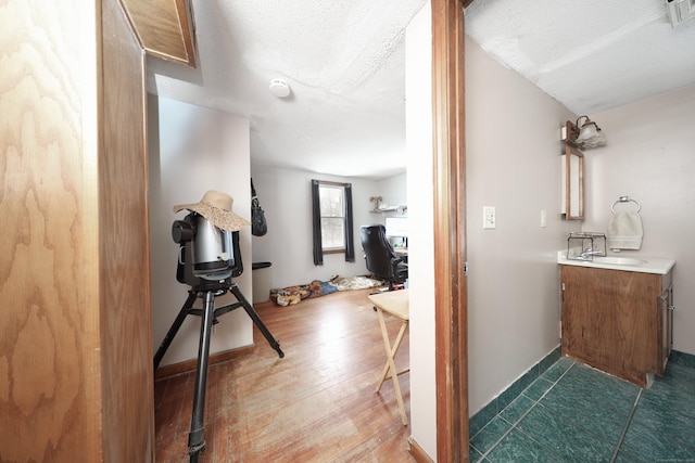 corridor with dark wood-style floors, visible vents, a sink, a textured ceiling, and baseboards