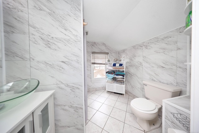 bathroom featuring lofted ceiling, toilet, tile patterned flooring, vanity, and tile walls