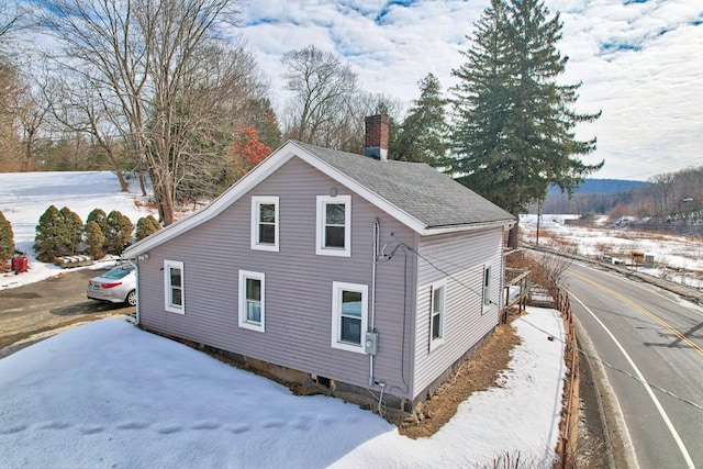 view of snow covered exterior featuring roof with shingles and a chimney