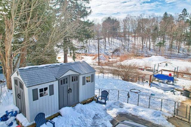 snow covered structure featuring an outbuilding, a storage unit, and fence