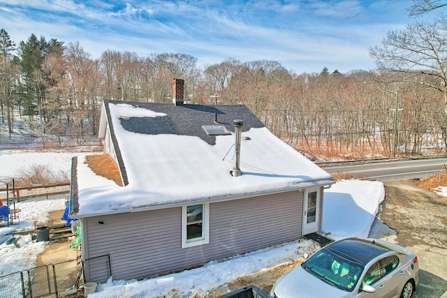 view of snowy exterior featuring roof with shingles, fence, and a chimney